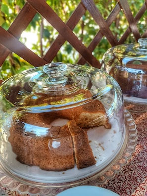 A glass-covered dessert stand with a cake on a white plate, set on a patterned tablecloth.