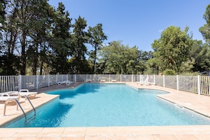 Una piscina rettangolare con recinzione bianca, circondata da alberi e dotata di sdraio.