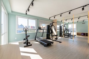 Ein modernes Fitnessstudio mit Cardiogeräten, Krafttrainingsgeräten und großen Fenstern mit Blick auf die Stadt.