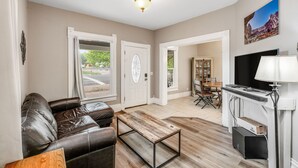 A living room with a leather sofa, a coffee table, a TV, and a lamp. There are two doors leading to other rooms. - 3BR near Downtown COS with fenced Backyard Seating (Colorado Springs)