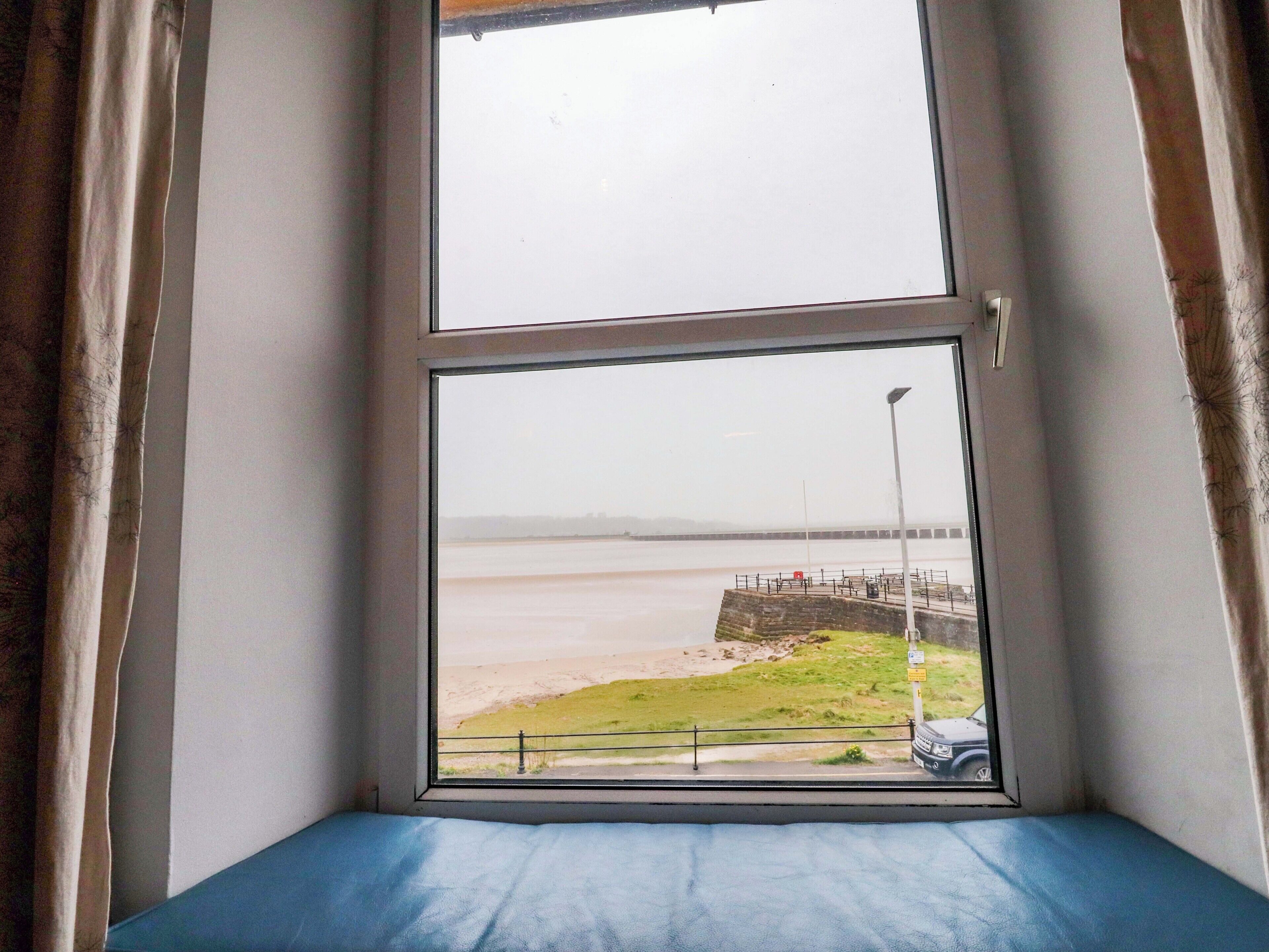 A room with a large window overlooking a beach and a pier.