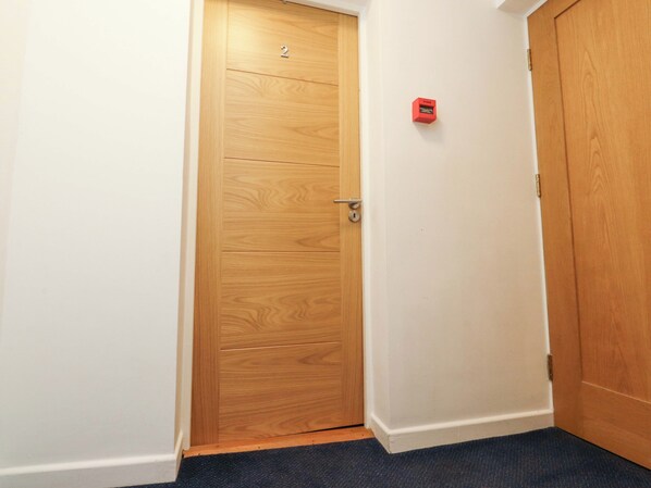 Una puerta de madera con el número 2 encima, un detector de incendios rojo en la pared y un suelo alfombrado.
