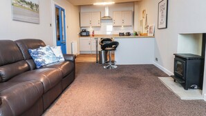 A living room with a brown leather sofa, a blue door, a kitchen with white cabinets, a black stove, and a framed quote on the wall. - Flat 2, Dorstan (Carnforth)