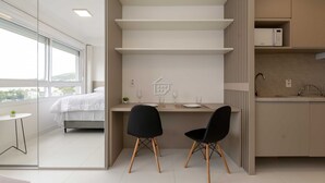 A modern bedroom with a bed, a small table with a plant, and a window. - Studio Cubanos | Hub Tecnológico + Lado da PUCRS (Porto Alegre)