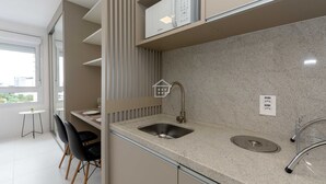 A modern kitchen with a built-in microwave, a sink, and a small dining area with chairs. - Studio Cubanos | Hub Tecnológico + Lado da PUCRS (Porto Alegre)