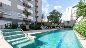 En swimmingpool med trappsteg som leder ner i vattnet, omgiven av grönska och en byggnad med balkonger.