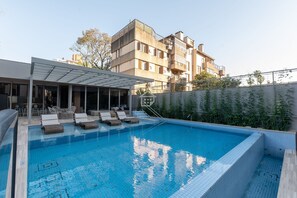 Ein Swimmingpool mit Liegestühlen, einer überdachten Sitzgelegenheit und einem Gebäude im Hintergrund.