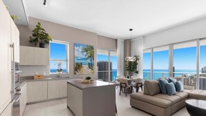 Un apartamento moderno con cocina, comedor y sala de estar, con amplias ventanas que ofrecen vista a la ciudad y al océano.