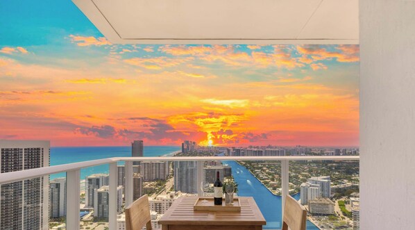 A balcony with a cityscape view, a table with a bottle and glasses, and a railing. - High Floor 2BR and 2 BA, Free Parking (Hollywood)
