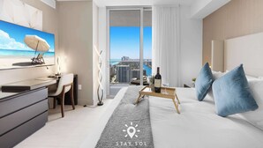Una habitación de hotel moderna con escritorio, silla, cama y vistas de la ciudad a través de amplias ventanas.