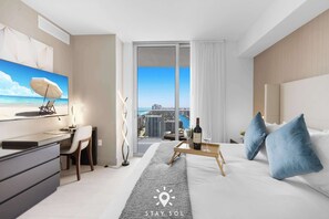A modern hotel room with a desk, chair, bed, and a view of the city through large windows. - High Floor 2BR and 2 BA, Free Parking (Hollywood)