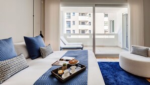 Quarto de hotel moderno com cama, bandeja de café da manhã, sofá e varanda com vista para edifícios.