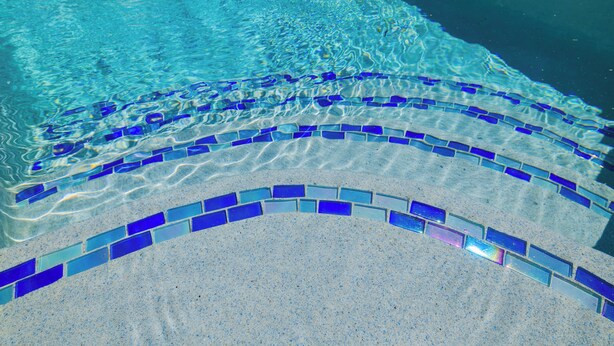 En klar pool med blå mosaikfliser og en sandbund.