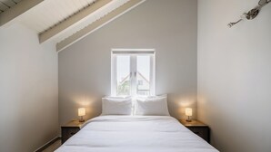 Et soveværelse med en seng, to sengeborde med lamper, et vindue og et skråt loft.