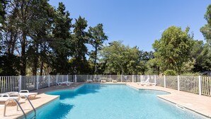 Ein rechteckiger Swimmingpool mit weißem Zaun, umgeben von Bäumen und mit Liegestühlen ausgestattet.