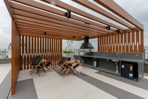 An outdoor patio with a wooden pergola, a grill station, and two folding chairs. - Studio Moderno com Vista para o Parque Farroupilha (Porto Alegre)