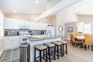 Una cocina moderna con armarios blancos, encimera de granito y una isla central con taburetes de bar.
