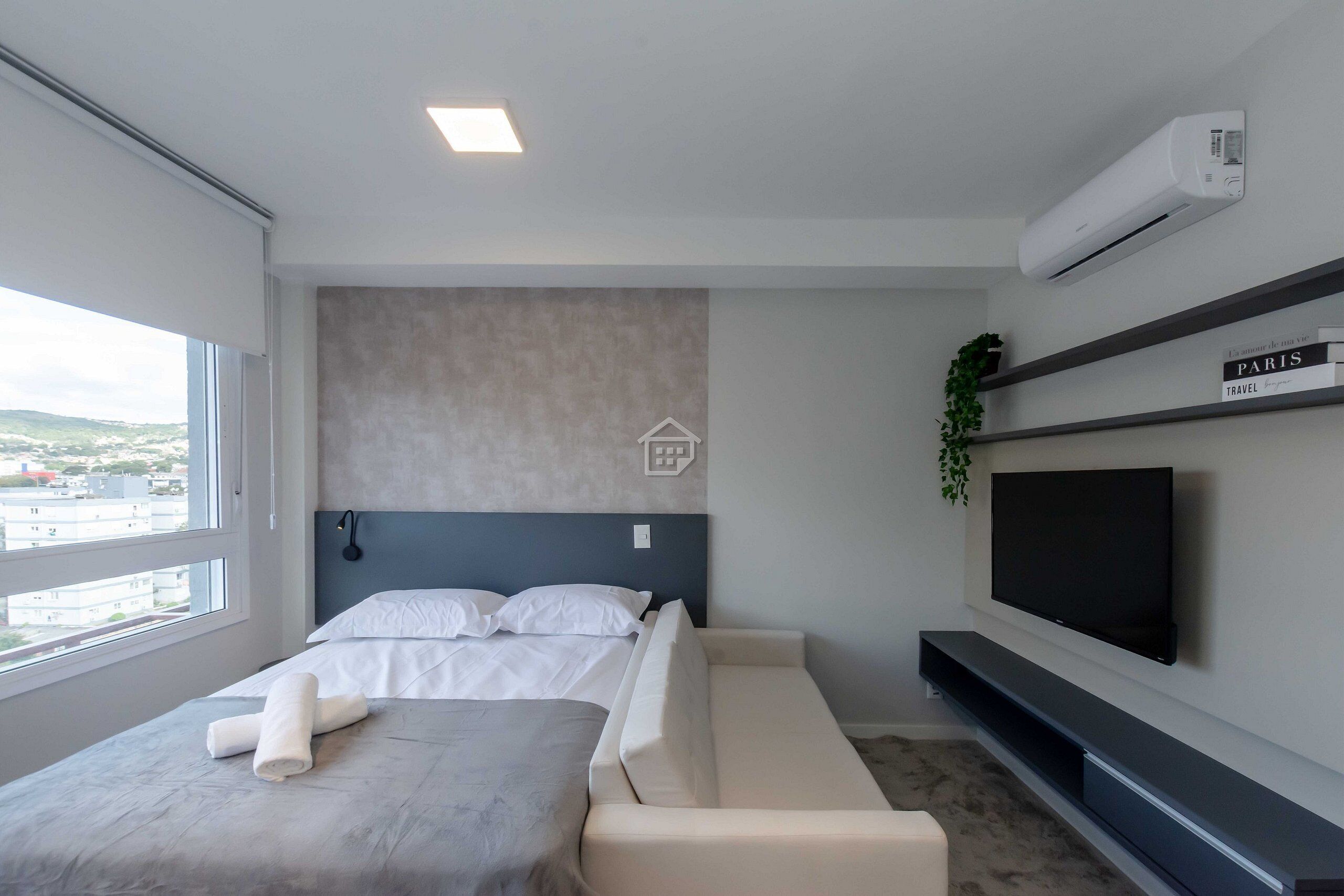 Una habitación de hotel moderna con cama, sofá, televisor y vistas a la ciudad.