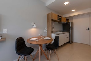 Cocina compacta con comedor, que incluye una mesa redonda con sillas, un refrigerador y una lámpara de pared.