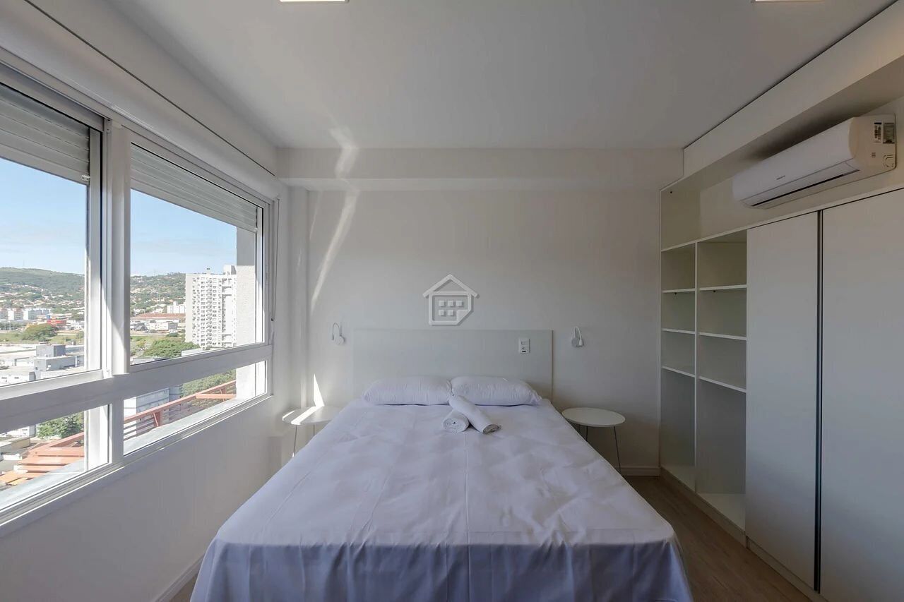 Une chambre à coucher comprenant un lit, une table de chevet, une petite table, une armoire et une fenêtre donnant sur la ville.