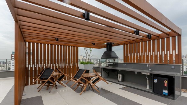 Un patio exterior con una pérgola de madera, una estación de parilla y dos sillas plegables.