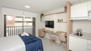 Habitació d'hotel moderna amb llit, escriptori, cadira, televisió i petita cuina.