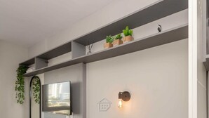 Un espace repas moderne avec une table ronde en bois, des chaises noires, un téléviseur à écran plat, un luminaire fixé au mur et un miroir.