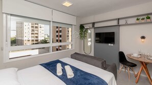 Une chambre d’hôtel moderne équipée d’un lit, d’une table à manger, d’une chaise, d’un téléviseur et d’une fenêtre donnant sur des immeubles.