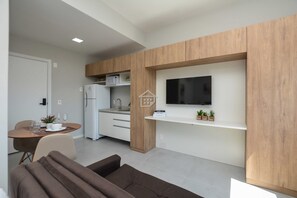 A modern kitchen with a built-in microwave, a dining area with a table and chairs, and a flat-screen TV mounted on a wooden wall. - Studio Moderno e Fluido de Frente para o Parque (Porto Alegre)
