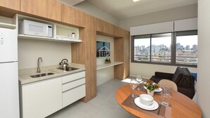 Una cucina moderna con forno a microonde, lavandino e bollitore, una zona pranzo con tavolo apparecchiato per due e vista sulla città attraverso ampie finestre.