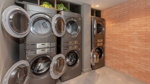 Una lavanderia dotata di diverse lavatrici, una parete in mattoni e una bocchetta di ventilazione al soffitto.