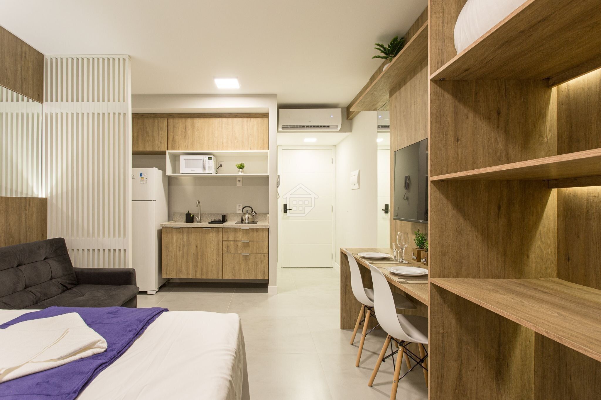 Una habitación moderna con cama, escritorio, kitchenette y televisión.