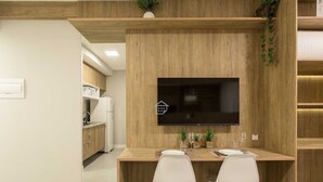 Une cuisine moderne avec des meubles en bois, un téléviseur encastré et un coin repas comprenant deux chaises blanches.
