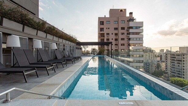 Une piscine sur le toit, dotée de chaises longues et d’une pergola, entourée d’immeubles de grande hauteur.