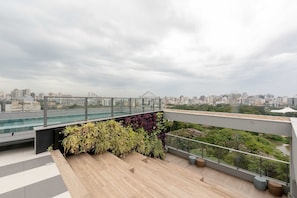 Terraço no telhado com vista para a cidade, guarda-corpo de vidro e parede verde.
