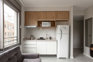 Une cuisine moderne avec des meubles en bois, un four à micro-ondes, un réfrigérateur et une fenêtre donnant sur des immeubles.
