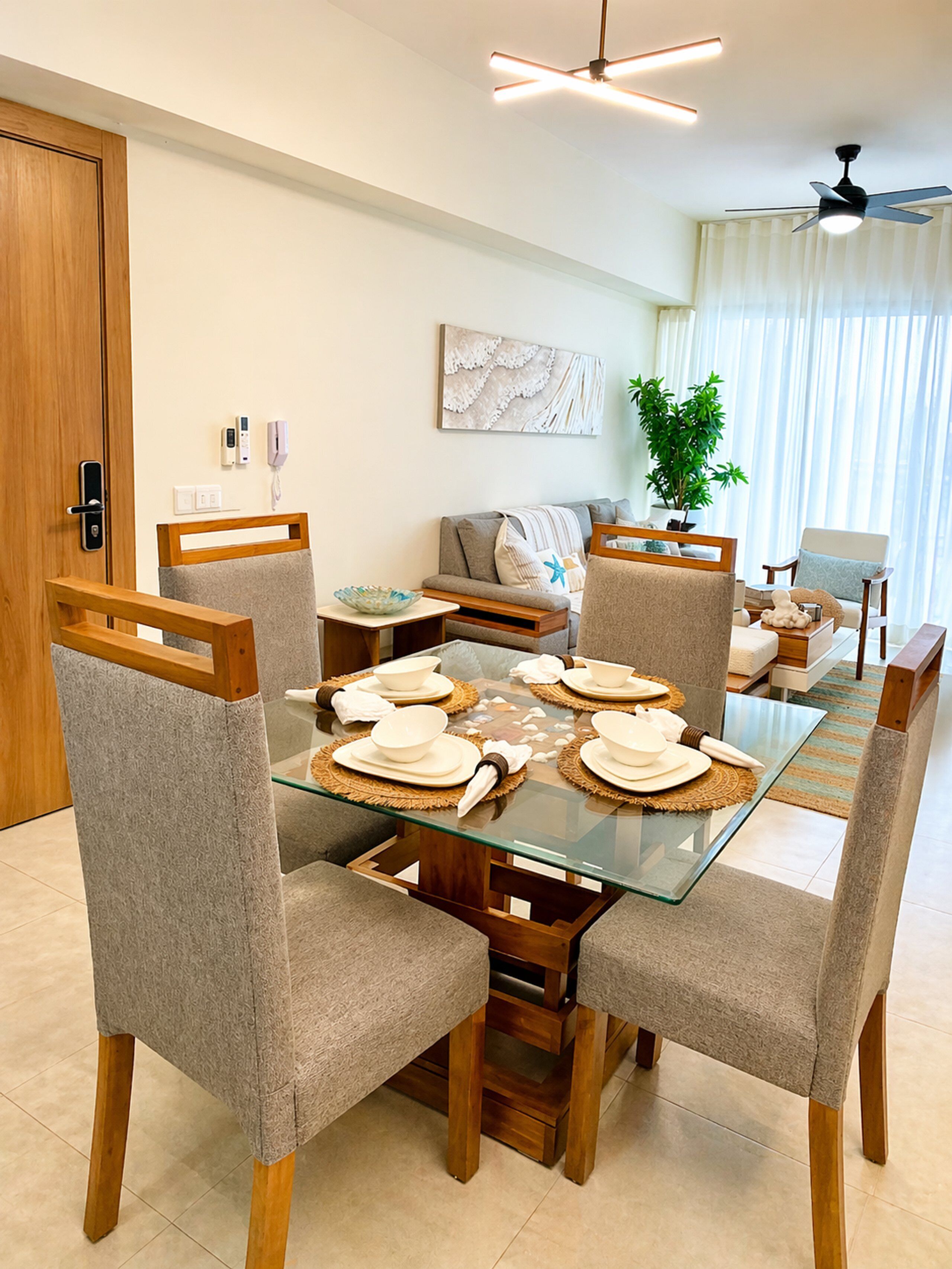 A dining area with a glass table, wooden chairs, and a sofa in the background.