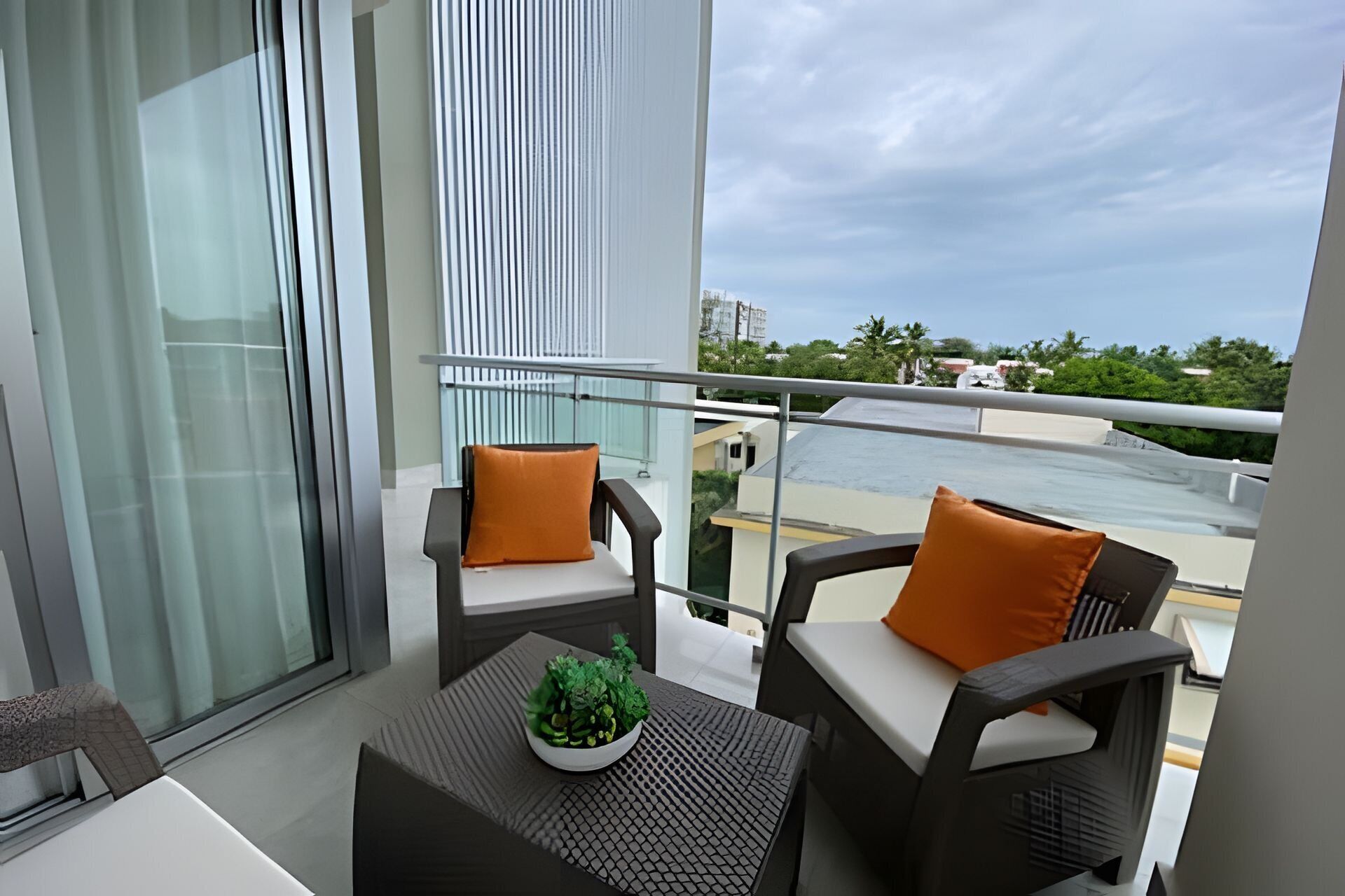 A balcony with two chairs, a small table with a plant, and a view of a river and buildings.