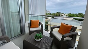 A balcony with two chairs, a small table with a plant, and a view of a river and buildings. - Apartamento Delicado Próximo a la Playa (Boca Chica)