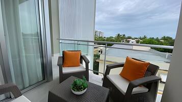 A balcony with two chairs, a small table with a plant, and a view of a river and buildings.