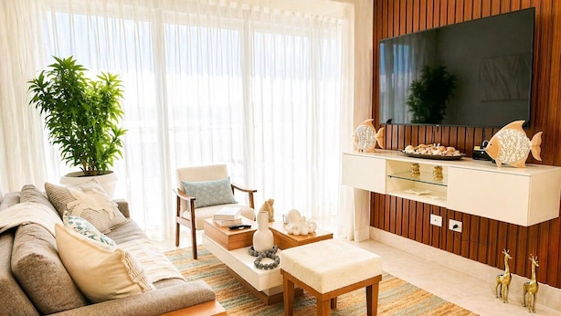 A living room with a sofa, armchair, coffee table, and a TV mounted on a wooden wall. - Apartamento Delicado Próximo a la Playa (Boca Chica)