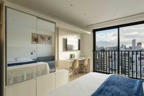 A modern hotel room with a bed, desk, and chairs, a city view, and a large window. - Studio Elegante e Conectado em Porto Alegre (Porto Alegre)