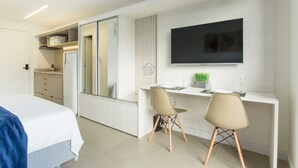 A modern hotel room with a bed, a desk with two chairs, a flat-screen TV, and a kitchenette. - Studio Elegante e Conectado em Porto Alegre (Porto Alegre)