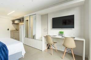 A modern hotel room with a bed, a desk with two chairs, a flat-screen TV, and a kitchenette. - Studio Elegante e Conectado em Porto Alegre (Porto Alegre)