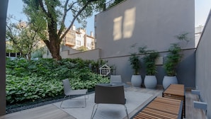 Eine moderne Terrassengrundstueck mit einer Holzbank, einem Tisch und Stühlen, umgeben von saftigem Grün und Topfpflanzen.