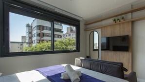 Ein Hotelzimmer mit Bett, großem Fenster, Fernseher und Blick auf Gebäude.