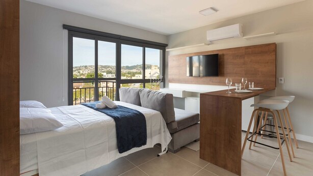 Een moderne hotelkamer met een bed, een kitchenette, een televisie en een balkon met uitzicht over de stad.