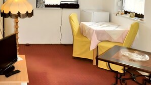 Huoneessa on televisio, lamppu, pöytä ja tuoli sekä ikkuna, jossa on sälekaihtimet.