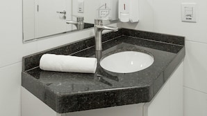 Un bagno moderno con un lavandino bianco, uno specchio grande e due dispenser di sapone.