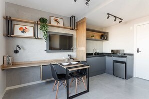 A modern kitchen with a built-in TV, wooden shelves, and a dining area with black chairs. - Studio Moderno com Vista e Lazer Completo (Porto Alegre)